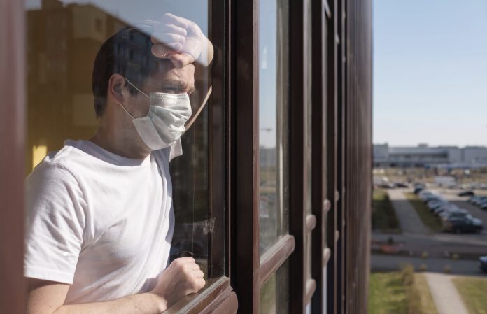 man with grippe looking through window and wearing mask protection